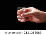 A glass of vodka in a man's hand. Black background. Copy space