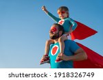 Small photo of Family of superheroes having fun outdoor. Father and son playing against blue summer sky background. Imagination and freedom concept