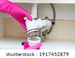 Small photo of Long hair and grime are the cause of a clogged sink. Plumber in pink rubber gloves clearing a clogged very dirty drain at home.