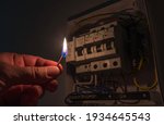 Blackout concept. Person's hand in complete darkness holding a burning match to investigate a home fuse box during a power outage.