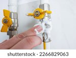 Small photo of A man applies soap foam to the connection of a gas valve and a flexible hose. A simple and cheap way to detect a gas leak in an apartment.