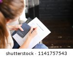 girl filling visa application form, student sitting on grey chair with passport. Young fair-haired woman wearing beige T-shirt jeans holding planchette with papers writing. Concept of execution of