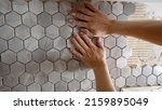 Small photo of The master glues a mosaic of ceramic tiles. The worker presses the tile with his hands while gluing the tile. The working tiler mounts the tile on the wall, presses it with his hands.