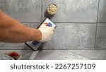 Small photo of Black grout for ceramic tiles. The master rubs the tile with a spatula. Repair and wall tiling. The master rubs the seams of the tiles with black putty with a rubber spatula.