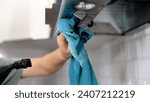 Small photo of A woman's hand washes the hood in the kitchen with a rag. Cleaning a household hood. Female hands cleaning a kitchen hood with a cloth. Woman wiping exhaust hood in kitchen, closeup.