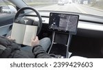 Small photo of Europe,Italy,Milan 12-11-2023 Autopilot and Self-Driving Features in Tesla Electric car - the car proceeds and the drive read a book, don t putting his hands on the steering wheel - assisted driving