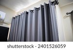 Small photo of dark grey curtains hanging from a curtain rod in a room. made of a heavy, possibly light-blocking material. silver grommets from a black curtain rod that is mounted to the wall.