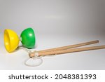 Yellow and green plastic diabolo with two wooden sticks and a white string ready to juggle on a white background