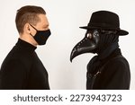 Small photo of A Plague doctor and a man in a Medical mask looking at each other. a syringe and needle with Medicine or serum, antidote. Isolated on a white background. COVID-19, epidemic and pandemic concept.