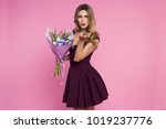 Small photo of Charming, pretty girl is holding a big tulip bouquet in hands. Lady is sending a vexed kiss. Pink background. Happy woman's day