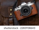 Camera in a brown leather case on a brown leather bag with a strap