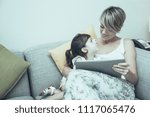 Small photo of Modern mother showing educational film to daughter. Pretty girl looking at mom. They relaxing on sofa in living room. Positive family using technology. Leisure concept