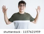 Small photo of Portrait of cheerful young Asian man in glasses raising hands. Vietnamese male student standing with surrendering gesture. Capitulation concept