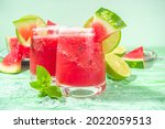 Cold summer cocktail, watermelon margaritas or mojito with watermelon and lime slices, crushed ice and mint. Seasonal refreshing drink, on bright green sun lighted background