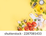 Cooking background with vegetable ingredients. Healthy dinner preparation flat lay, with fresh raw tomatoes, onion, garlic, herbs and greens, olive oil, salt, pepper seasonings, on yellow background 