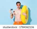 Small photo of Surprised young man guy in eyeglasses isolated on pastel blue wall background studio portrait. People summer vacation rest lifestyle concept. Mock up copy space. Hold inflatable ring credit bank cank