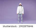 Full length of smiling attractive man in warm white padded windbreaker jacket hat standing looking camera isolated on purple background studio portrait. People lifestyle cold winter season concept