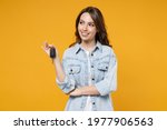 Young smiling dreamful pensive wistful happy rich brunette woman 20s wearing stylish denim shirt white t-shirt holding in hands car keys look aside isolated on yellow color background studio portrait
