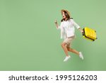 Full length traveler tourist woman in casual clothes straw hat jump high hold suitcase run isolated on pastel green background. Passenger travel abroad on weekends getaway. Air flight journey concept
