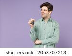 Young smiling satisfied dreamful happy fun man in casual green mint shirt white t-shirt holding car key fob keyless system look aside isolated on purple background studio portrait. Lifestyle concept