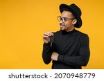 Small photo of Young happy thoughtful dreamful wistful fun american african man 20s wear stylish black shirt hat eyeglasses holding car key looking aside isolated on yellow orange color background studio portrait.