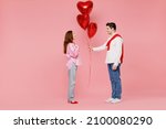 Full body side view young couple two friends woman man 20s in shirt hold bunch of red inflatable balloons isolated on plain pastel pink background studio Valentine's Day birthday holiday party concept