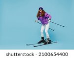Full body skier shocked happy fun cool woman 20s wearing warm purple padded windbreaker jacket ski goggles mask spend extreme weekend in mountains look camera isolated on plain blue background studio.