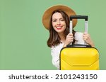 Close up cheerful fun traveler tourist woman in casual clothes hat hiding with yellow suitcase valise isolated on green background Passenger travel abroad weekends getaway Air flight journey concept.