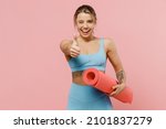 Young strong sporty athletic fitness trainer instructor woman wear blue tracksuit spend time in home gym show thumb up gesture blink isolated on pastel plain pink background. Workout sport concept.