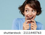 Small photo of Close up young happy woman in casual sweater hold sweet pink cream donuts biting chocolate bar look camera isolated on plain pastel light blue background studio portrait. People lifestyle food concept