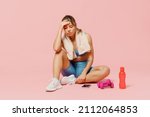 Small photo of Full body young strong sporty athletic fitness trainer instructor woman wear blue tracksuit spend time in home gym sit on floor hold head isolated on plain light pink background. Workout sport concept