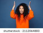 Small photo of Angry irritated young african american woman wearing casual basic bright orange sweatshirt standing spreading hands screaming swearing looking camera isolated on blue color background studio portrait