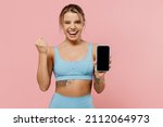 Small photo of Young sporty athletic fitness trainer instructor woman wear tracksuit spend time in home gym hold mobile cell phone blank screen area do winner gesture isolated on plain pink background Sport concept