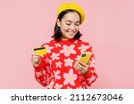 Small photo of Woman of Asian ethnicity 20s wear red knitted sweater beret using mobile cell phone hold credit bank card doing online shopping order delivery booking tour isolated on plain pastel pink background.