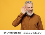 Small photo of Curious nosy smiling excited elderly gray-haired bearded man 40s years old wears brown shirt look aside try to hear you overhear listening intently isolated on plain yellow background studio portrait