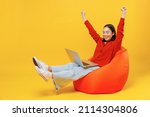 Small photo of Full size body length young woman of Asian ethnicity 20s in casual clothes sit in bag chair hold use work on laptop pc computer doing winner gesture isolated on plain yellow background studio portrait