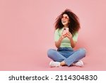 Full size young curly latin woman 20s wears casual clothes sit hold use mobile cell phone look aside on workspace area copy space mock up isolated on plain pastel light pink background studio portrait