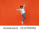 Full size body length smiling young bearded Indian man 20s years old wears blue shirt standing on toes dancing lean back have fun spreading hands isolated on plain orange background studio portrait