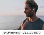 Close up side view young strong athletic toned fit sportsman man in sports clothes earphones warm up train with music at sunrise sun dawn over sea beach outdoor on pier seaside in summer day morning.