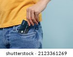 Small photo of Cropped close up rich man 20s wearing yellow t-shirt hold in hand put credit bank card to jeans denim pocket isolated on plain pastel light blue background studio portrait. People lifestyle concept.