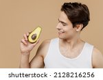 Small photo of Attractive smiling happy fun young man he 20s perfect skin in undershirt hold half of avocado isolated on pastel light beige background studio portrait Skin care healthcare cosmetic procedures concept