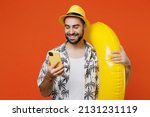 Small photo of Young smiling happy tourist man in beach shirt hat hold inflatable ring hold in hand use mobile cell phone isolated on plain orange background studio portrait. Summer vacation sea rest sun tan concept