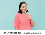 Young smiling fun happy woman of Asian ethnicity 20s wearing pink sweater showing thumb up like gesture isolated on pastel plain light blue color background studio portrait. People lifestyle concept