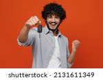 Charming fun young bearded Indian man 20s years old wears blue shirt hold in hand new car key doing winner gesture celebrate clenching fists say yes isolated on plain orange background studio portrait