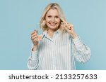 Small photo of Elderly happy woman 50s wear casual striped shirt hold glass of water medication tablets, aspirin pills isolated on plain pastel light blue color background studio portrait. People lifestyle concept
