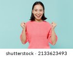 Small photo of Young smiling happy excited woman of Asian ethnicity 20s wear pink sweater doing winner gesture celebrate clenching fists say yes isolated on pastel plain light blue color background studio portrait.