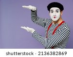 Small photo of Charismatic amazing ecstatic young mime man with white face mask wears striped shirt beret hands aside like holding carrying something isolated on plain pastel light violet background studio portrait