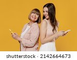 Small photo of Side view two fun young daughter mother together couple women in casual clothes hold mobile cell phone stand back to back look to each other isolated on plain yellow background studio Family concept