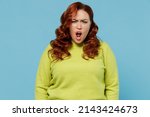 Small photo of Young indignant angry sad swearing offended chubby overweight plus size big fat fit woman wear green sweater scream shout isolated on plain blue background studio portrait. People lifestyle concept