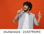 Small photo of Young bearded Indian man 20s years old wears blue shirt sing song in microphone dance sing song fooling around have fun gesticulating hands enjoy isolated on plain orange background studio portrait